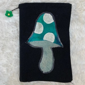 Könnte beinhalten: Schwarze Canvas-Kosmetiktasche mit einem grünen und weißen Pilz-Applikationen. Der Pilz hat weiße Punkte.