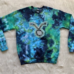 May include: A blue, green and white tie-dye sweatshirt with a turquoise Taurus zodiac sign patch on the front.
