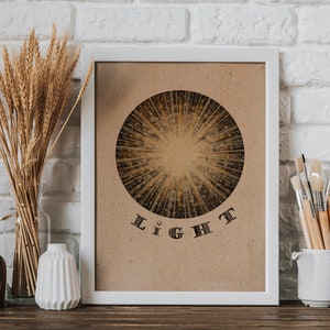 May include: A white framed print with a brown background featuring a circular design of radiating lines in gold and black. The word "LIGHT" is printed in black below the circle.