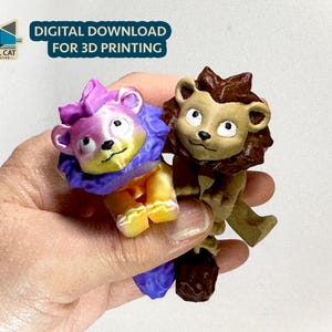 Op de afbeelding: Twee 3D-geprinte leeuwenfiguren. Eén is een lichtbruine leeuw met een manen. De andere is een paarse en gele leeuw met een manen. De leeuwen houden elkaar vast.
