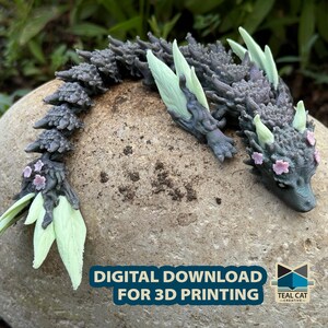 Puede incluir: Un modelo impreso en 3D de un pequeño dragón gris con alas verdes y flores rosas. El dragón está enroscado en una roca gris. El texto "DESCARGA DIGITAL PARA IMPRESIÓN 3D" es visible en la parte inferior de la imagen.