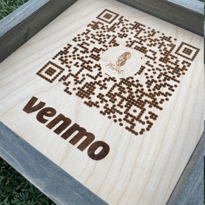 May include: A wooden sign with a gray frame and a laser-engraved QR code. The sign also has the word "venmo" engraved on it.
