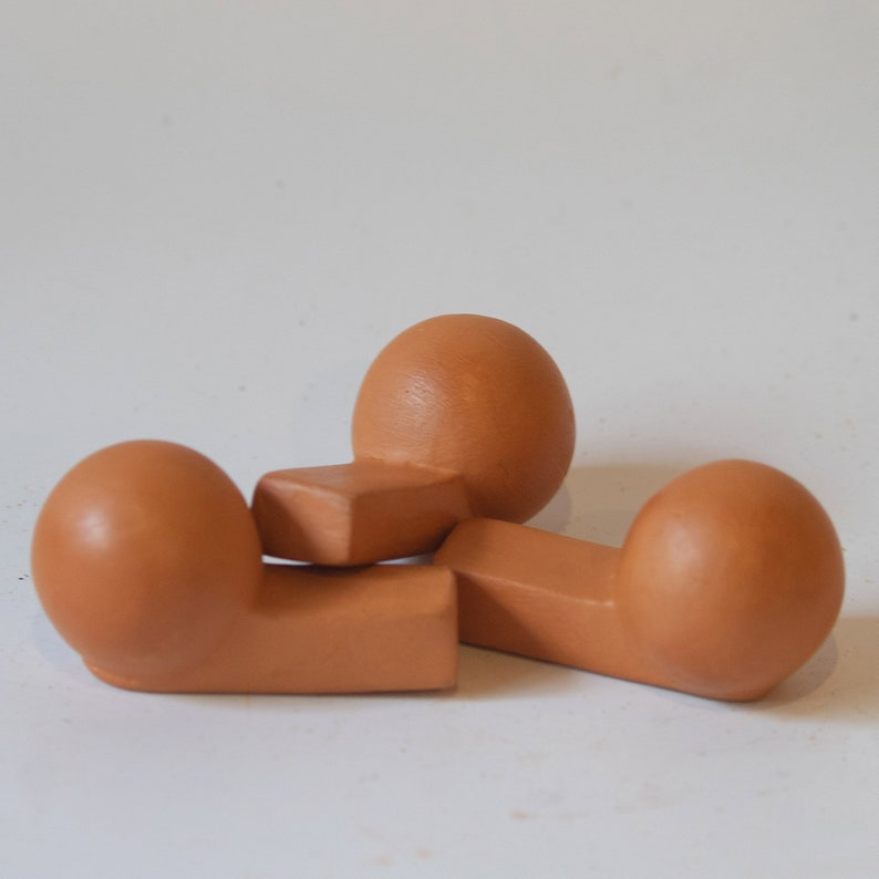 May include: Three terracotta-colored ceramic sculptures in the shape of rounded, abstract forms. The sculptures are arranged in a triangular formation.