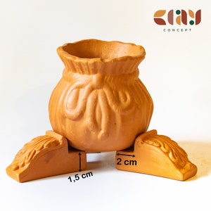 May include: Terracotta planter shaped like a bag with three legs. The planter is 1.5 inches tall and 2 inches wide.  CLAY CONCEPT.
