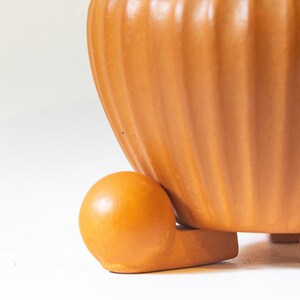 May include: A terracotta-colored ceramic planter with a ribbed design and a rounded base. The planter has a smooth, glossy finish and is perfect for displaying plants or flowers.
