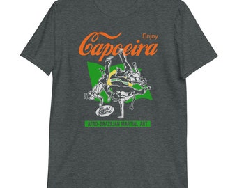 Può includere: Una t-shirt grigio scuro melange con una grafica di persone che praticano la capoeira, un'arte marziale brasiliana. Il testo "Enjoy Capoeira" è in arancione e il testo "Fight & Dance Afro-Brazilian Martial Art" è in verde.