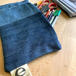 May include: A blue denim pencil case with a white label that says "eric & edwin" and a stylised letter "e" on it.
