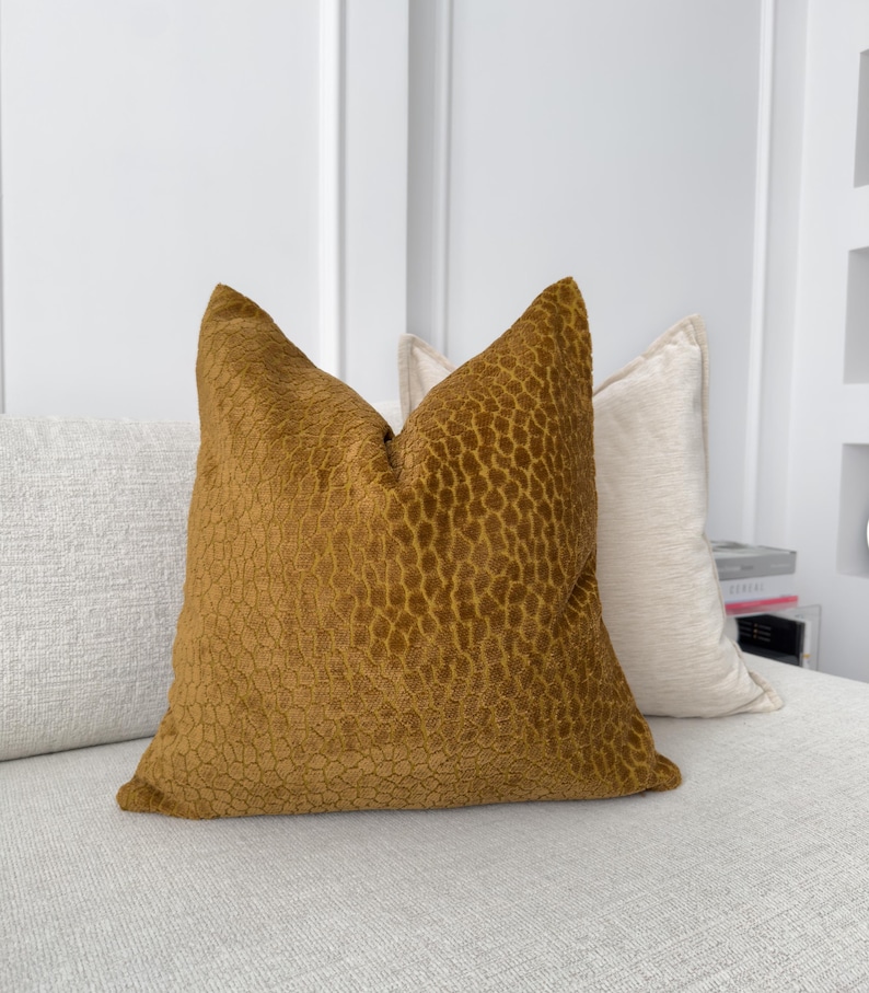 K&ouml;nnte beinhalten: Ein senfgelbes Kissen mit einem strukturierten, geometrischen Muster. Das Kissen liegt auf einem wei&szlig;en Sofa.