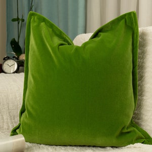May include: A bright green velvet pillow with a smooth, soft texture. The pillow is placed on a white, textured surface.