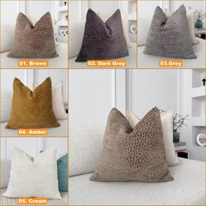 Puede incluir: Cojines decorativos en marr&oacute;n, gris oscuro, gris, &aacute;mbar y crema. Cada coj&iacute;n presenta un patr&oacute;n texturizado y se muestra en un sof&aacute; de color neutro. La imagen incluye etiquetas de texto que indican el color de cada coj&iacute;n.