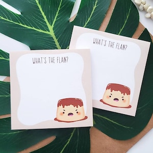 May include: Two square sticky note pads with a light beige border and a white center. Each note features the text "WHAT'S THE FLAN?" at the top and a cartoon illustration of a brown flan dessert with a grumpy facial expression at the bottom.