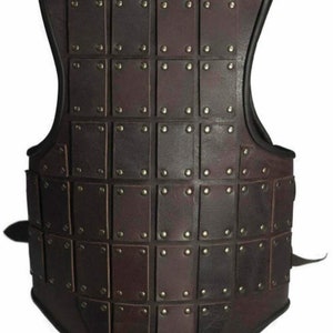May include: A brown leather vest with a grid pattern of square leather plates, each secured with a metal rivet. The vest has a black trim around the neckline and armholes.