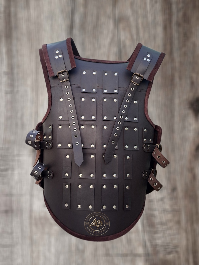 May include: A brown leather armour vest with metal rivets and straps. The vest has a rounded bottom and a logo that says "A.P. Handicraft".