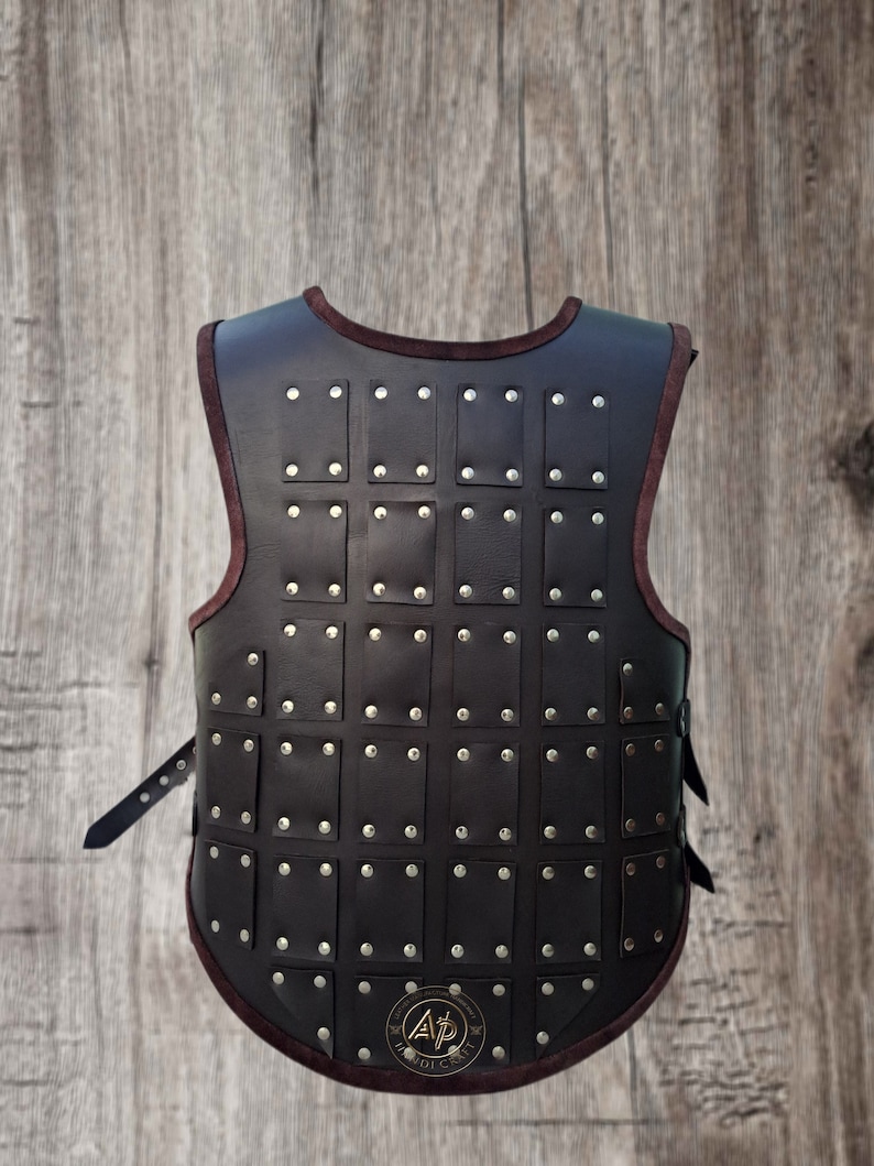 May include: A brown leather vest with a decorative pattern of metal studs. The vest has a strap on each side and a logo on the back.