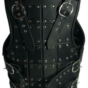 May include: Black leather armour with metal rivets and buckles. The armour is made of multiple leather panels that are stitched together. The armour has a strap that goes over the shoulders and buckles at the front.
