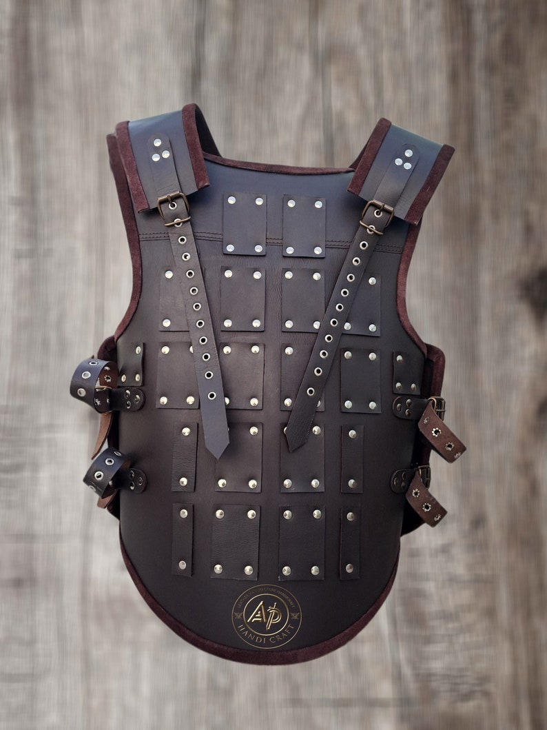 May include: A brown leather armour vest with metal rivets and straps. The vest has a rounded bottom and a logo that says "A.P. Handicraft".