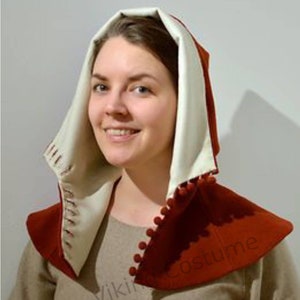 May include: A red and white hooded cloak with a white lining and a row of white pom-poms around the edge. The hood is pulled up over the head of the person wearing it.
