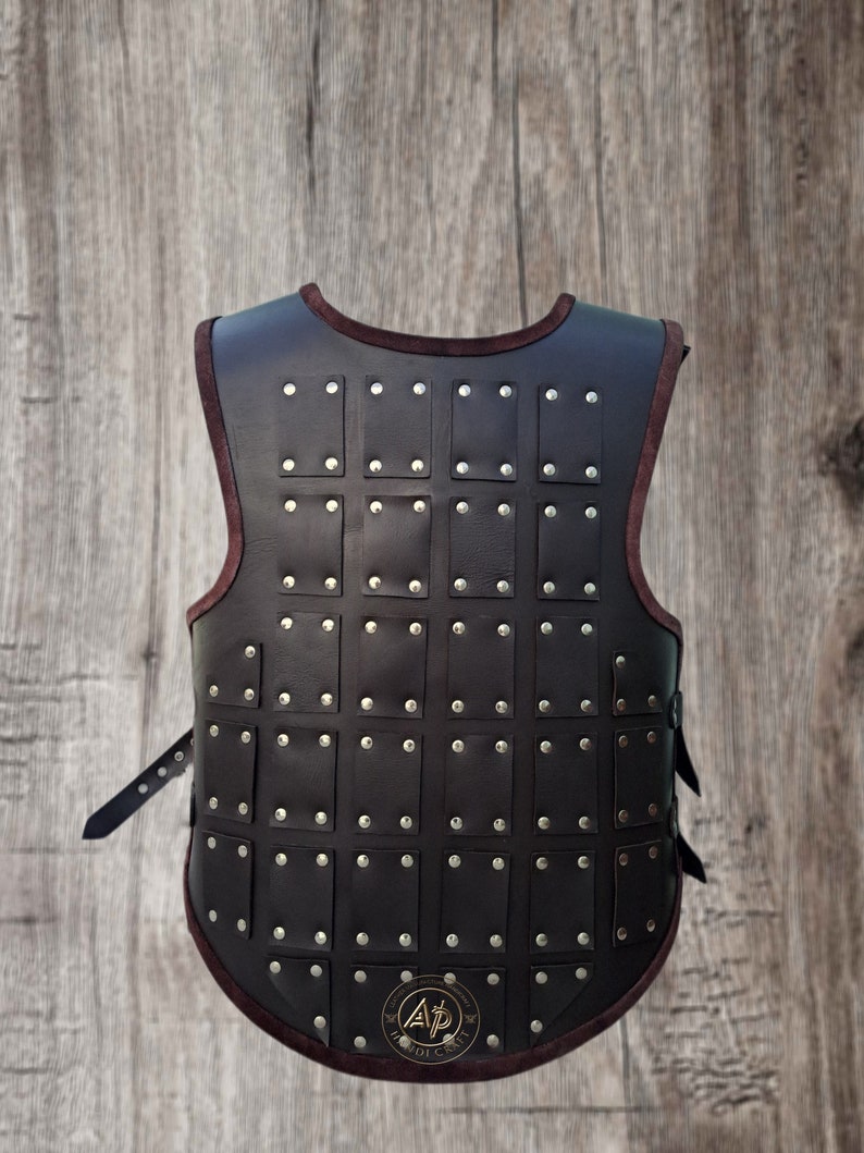 May include: A brown leather vest with a decorative pattern of metal studs. The vest has a strap on each side and a logo on the back.