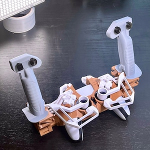 May include: A 3D printed gaming controller with two white joysticks and a white trigger. The controller is made of brown and white plastic and has a white and grey design. The controller is sitting on a black surface.