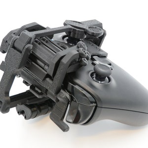 May include: A black Xbox controller with a 3D printed attachment that adds extra buttons and a thumbstick to the top of the controller.