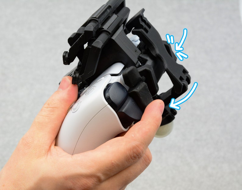 Puede incluir: Un accesorio de agarre para tel&eacute;fono de pl&aacute;stico negro para un mando de juego blanco. El agarre tiene una correa que se puede ajustar para adaptarse a diferentes tama&ntilde;os de mano. El agarre est&aacute; dise&ntilde;ado para fijarse en la parte posterior del mando, proporcionando un agarre m&aacute;s seguro.