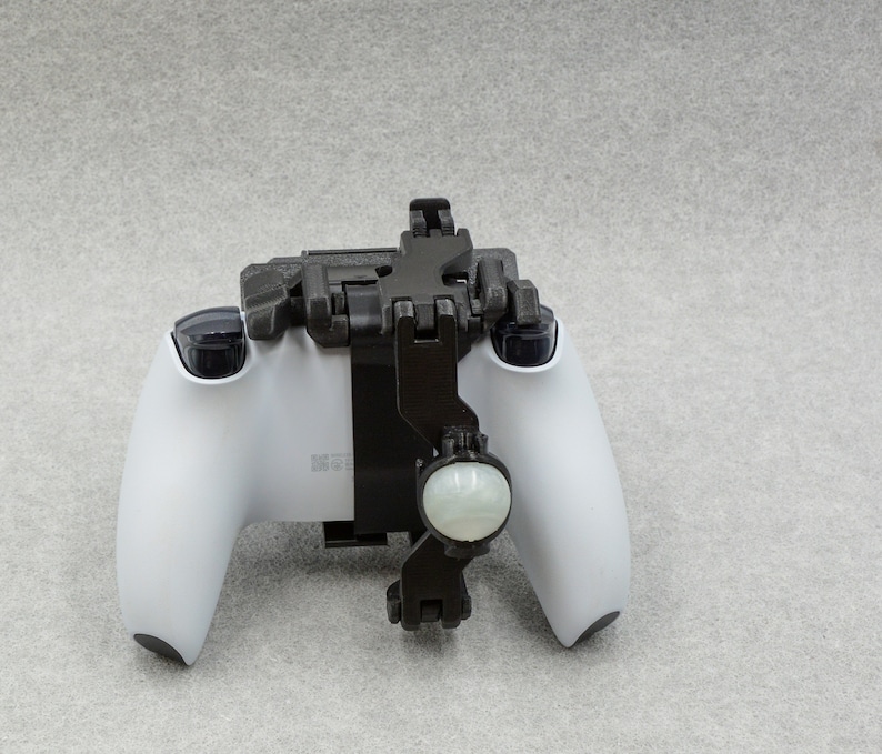 Puede incluir: Un mando de videojuegos blanco con un accesorio de pl&aacute;stico negro. El accesorio tiene un bot&oacute;n redondo blanco en la parte delantera.