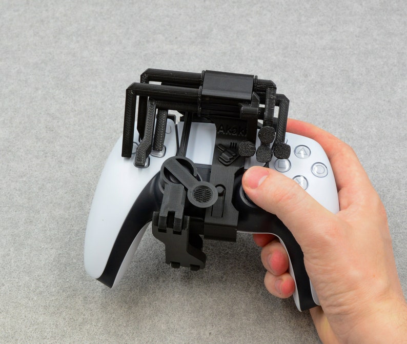 Puede incluir: Un accesorio de agarre para mando negro impreso en 3D para un mando PlayStation 5 DualSense blanco. El agarre tiene una superficie texturizada y est&aacute; dise&ntilde;ado para mejorar el agarre del usuario en el mando.