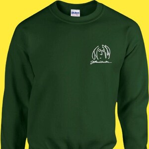 Puede incluir: Una sudadera verde oscuro con un contorno blanco de la cara y la firma de John Lennon.
