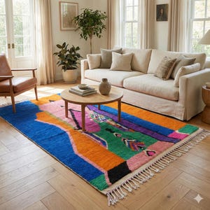 May include: A colorful area rug with a vibrant geometric design. The rug features a bold combination of blue, orange, pink, green, and purple hues. It has a fringed edge and is placed in a living room setting with a sofa and coffee table.