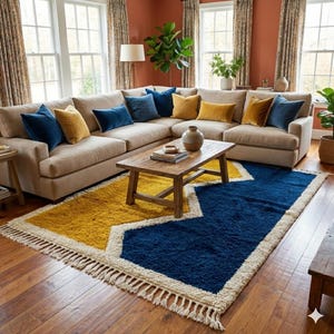 Peut inclure: Un canapé d'angle beige avec des coussins bleu marine et dorés. Une table basse en bois repose sur un tapis géométrique avec des sections jaunes, bleu marine et blanches. Le tapis a une bordure à franges. La pièce a de grandes fenêtres et des murs aux tons chauds.