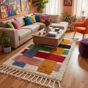 May include: A living room scene featuring a beige sectional sofa, colorful throw pillows, and a wooden coffee table. A vibrant, rectangular rug with a geometric pattern of red, yellow, blue, and green blocks sits on the wooden floor. The room is decorated with artwork and plants.