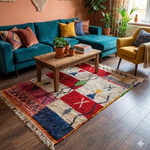 May include: A vibrant, rectangular rug with a patchwork design. The rug displays red, white, blue, and green geometric patterns. It is placed on a dark wood floor in a living room setting, with a teal sofa and wooden coffee table.
