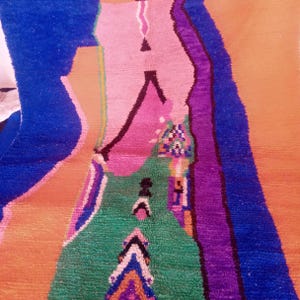 May include: A colorful, abstract rug with a geometric design. The rug features a vibrant mix of colors, including blue, pink, green, purple, and orange. The design includes various shapes and patterns, creating a visually striking piece. The rug is likely made of wool or a similar material.
