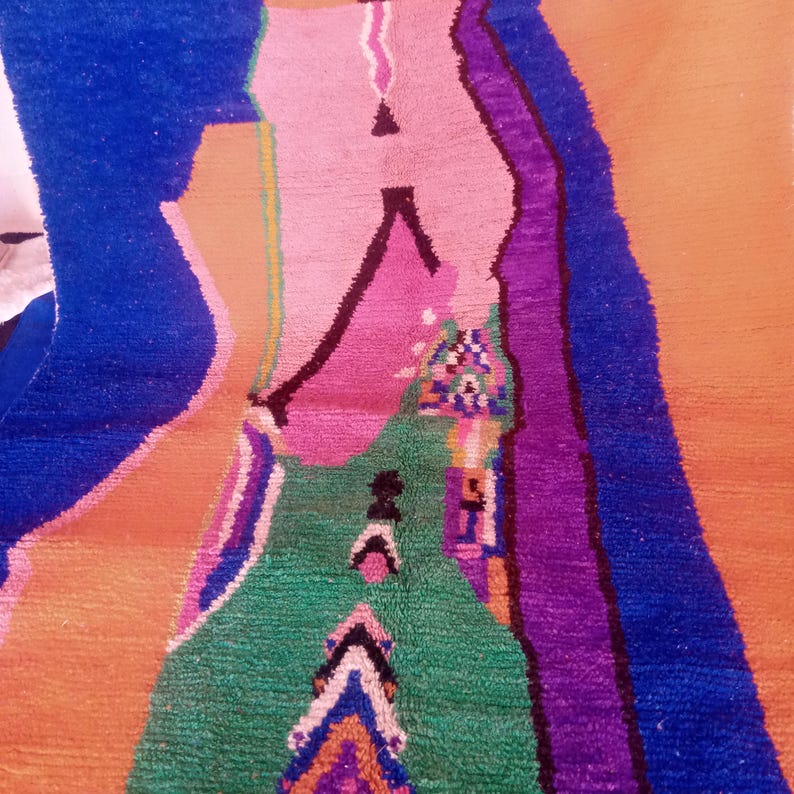 May include: A colorful, abstract rug with a geometric design. The rug features a vibrant mix of colors, including blue, pink, green, purple, and orange. The design includes various shapes and patterns, creating a visually striking piece. The rug is likely made of wool or a similar material.