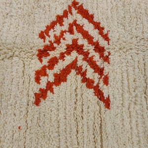 K&ouml;nnte beinhalten: Cremefarbener Teppich mit strukturierter Oberfl&auml;che und einem kr&auml;ftigen, geometrischen Design in Orange- und Wei&szlig;t&ouml;nen. Das Muster zeigt eine Reihe von pfeilartigen Formen, die einen auff&auml;lligen visuellen Kontrast erzeugen. Geeignet f&uuml;r Wohn- und Schlafzimmer.