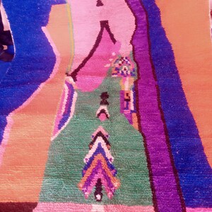 May include: A colorful, patterned rug with a geometric design. The rug features a combination of vibrant colors, including blue, pink, green, purple, and orange. The design includes arrow-like shapes and other abstract patterns, creating a visually striking textile.