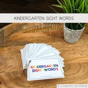 May include: A set of colorful flash cards with the words "Kindergarten Sight Words" printed on the front. The cards are arranged in a fan shape and have a silver ring binder.