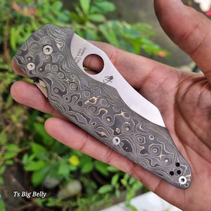 May include: A black and gold patterned pocket knife with a silver blade. The knife has a hole in the handle and the text "G. SAK. USA" is engraved on the handle.