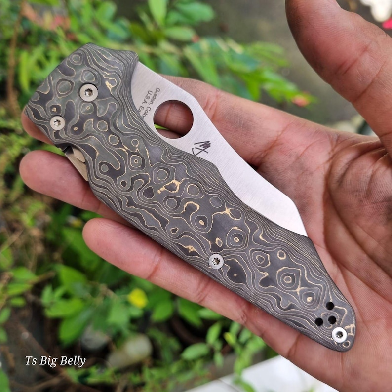 May include: A black and gold patterned pocket knife with a silver blade. The knife has a hole in the handle and the text "G. SAK. USA" is engraved on the handle.
