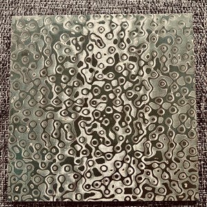May include: A close-up of a metal sheet with a swirling pattern of black and white circles and lines. The metal has a textured surface.