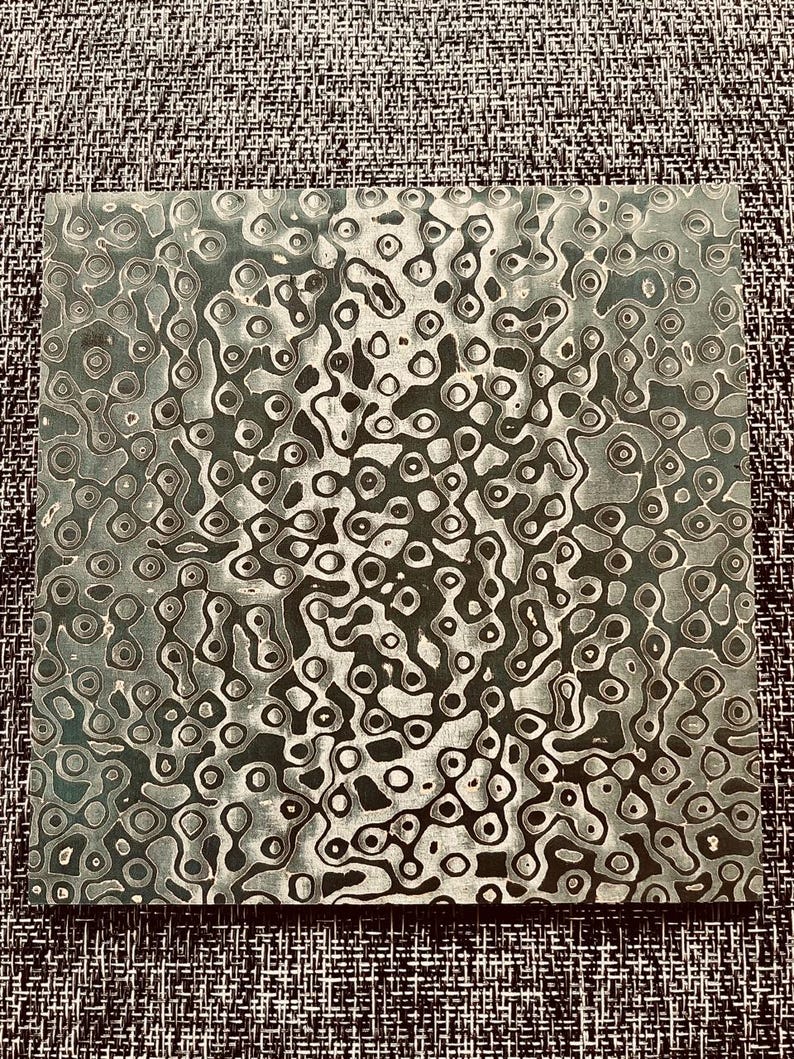 May include: A close-up of a metal sheet with a swirling pattern of black and white circles and lines. The metal has a textured surface.