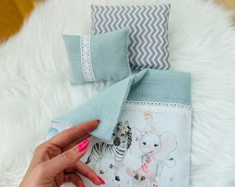 May include: A light blue and white doll bed with a white and gray patterned pillow, a light blue pillow with white lace trim, and a white sheet with a colorful animal print. The sheet features a zebra, an elephant, a lemur, and a bird.
