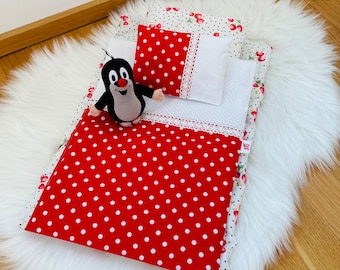 May include: A red and white polka dot doll bed with a white pillow and a stuffed mole toy. The bed is on a white fluffy surface.