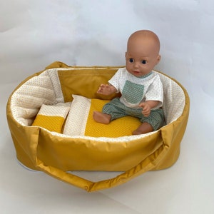 May include: A yellow and white patterned doll bed with a doll wearing a green and white polka dot outfit sitting inside.