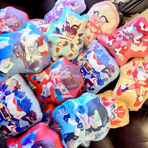 May include: A collection of colorful plush pillows featuring various cartoon characters. The pillows are made of soft, plush fabric and feature different designs, including robots, animals, and other characters.