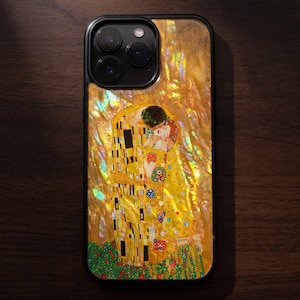 May include: A smartphone case featuring a reproduction of Gustav Klimt's The Kiss painting. The design is set against a shimmering, iridescent gold background with a pearlescent texture. The case has a black frame and a triple-lens camera cutout.