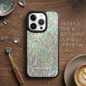 May include: A smartphone case featuring an iridescent abalone shell pattern with a black camera housing. The text "casetimy" is printed in white script at the bottom. To the right, the text "SELECT YOUR CUSTOM NAME & COLOR" is visible.