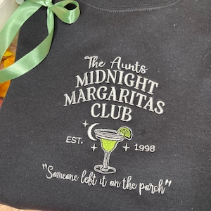 May include: Dark grey sweatshirt with white embroidered text: "The Aunts Midnight Margaritas Club" and a margarita glass graphic. Includes "EST. 1998" and the quote, "Someone left it on the porch."