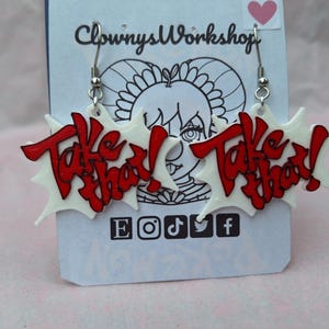 May include: A pair of white and red earrings with the words "Take That!" on each earring. The earrings are shaped like a starburst.