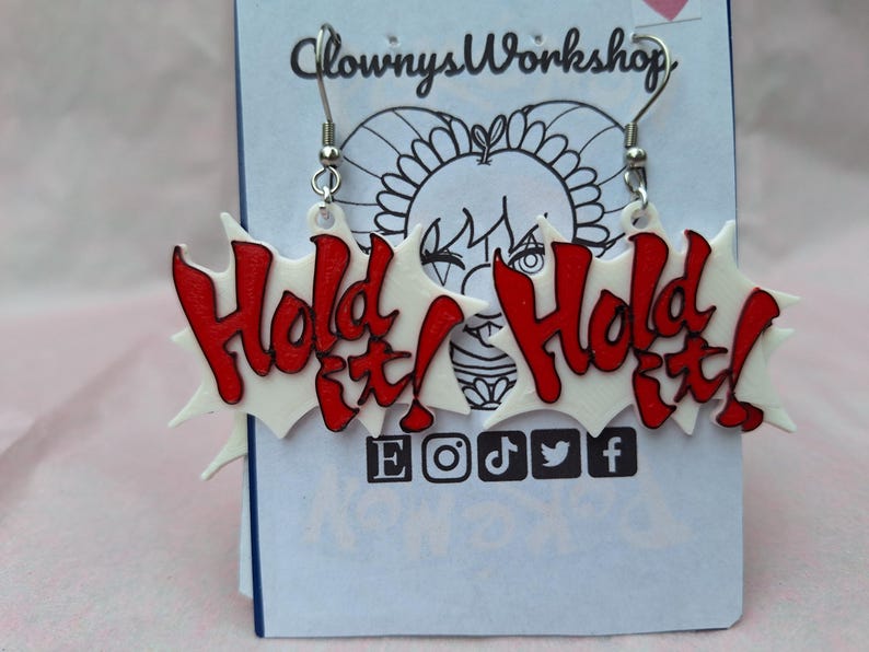 May include: A pair of white and red earrings with the words "Hold It!" on each earring. The earrings are made of acrylic and have silver hooks.